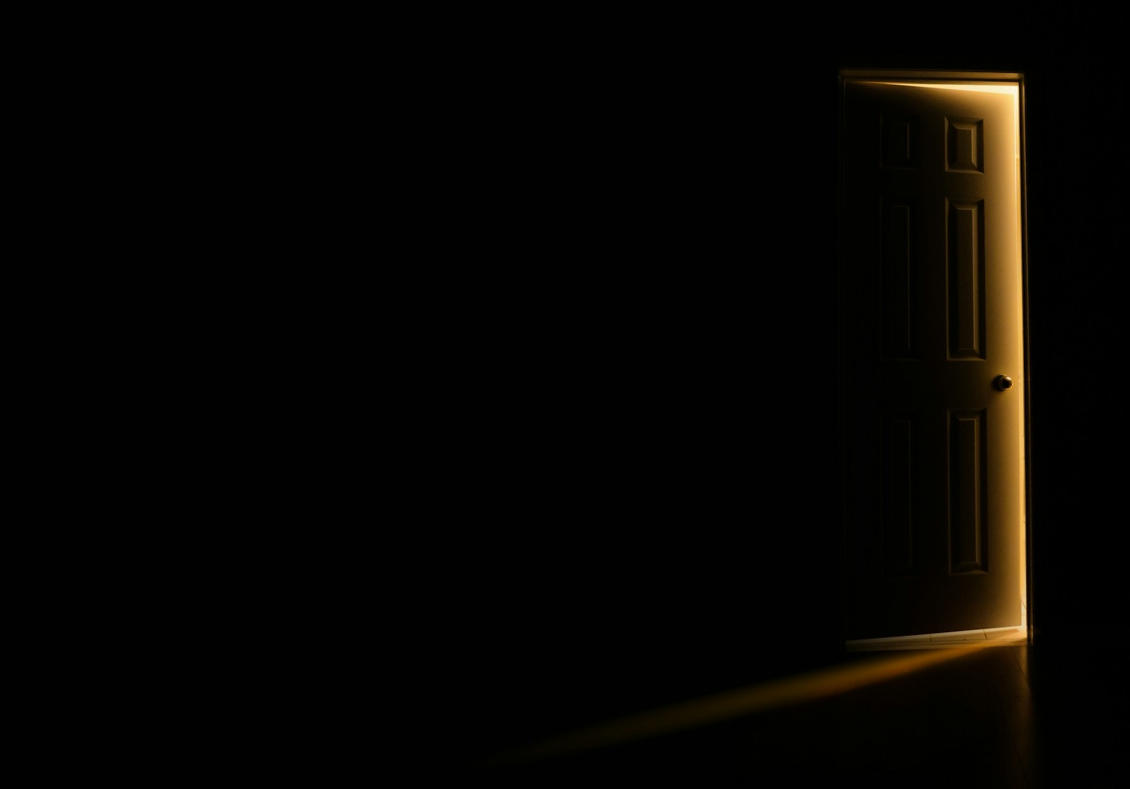 A door standing slightly open in a dark room, warm light spilling through the gap