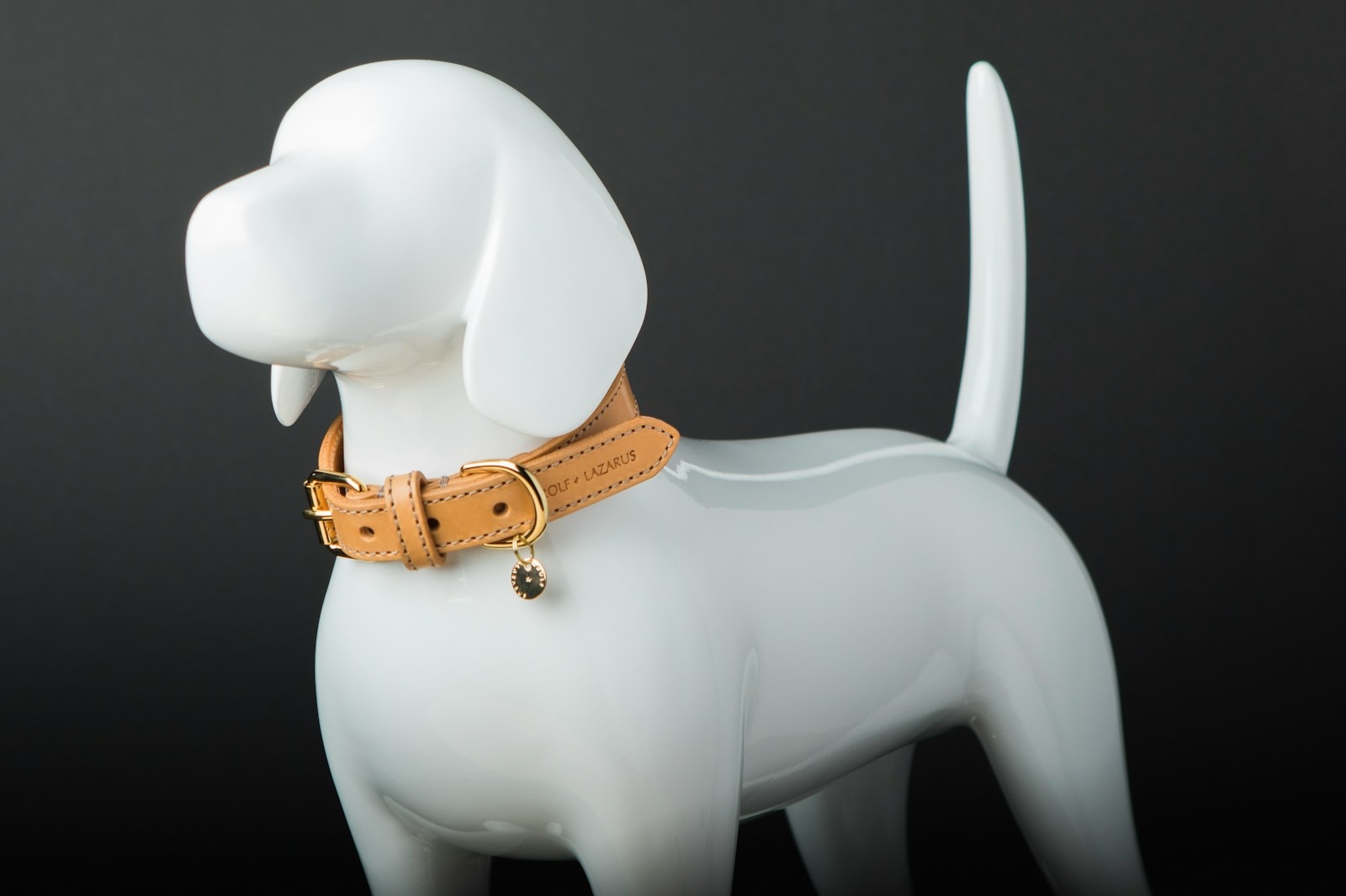A white ceramic dog figure wearing a tan leather collar against a dark background