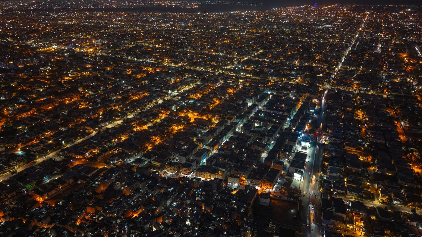 An aerial view of a city at night, its streets traced in orange and white lights
