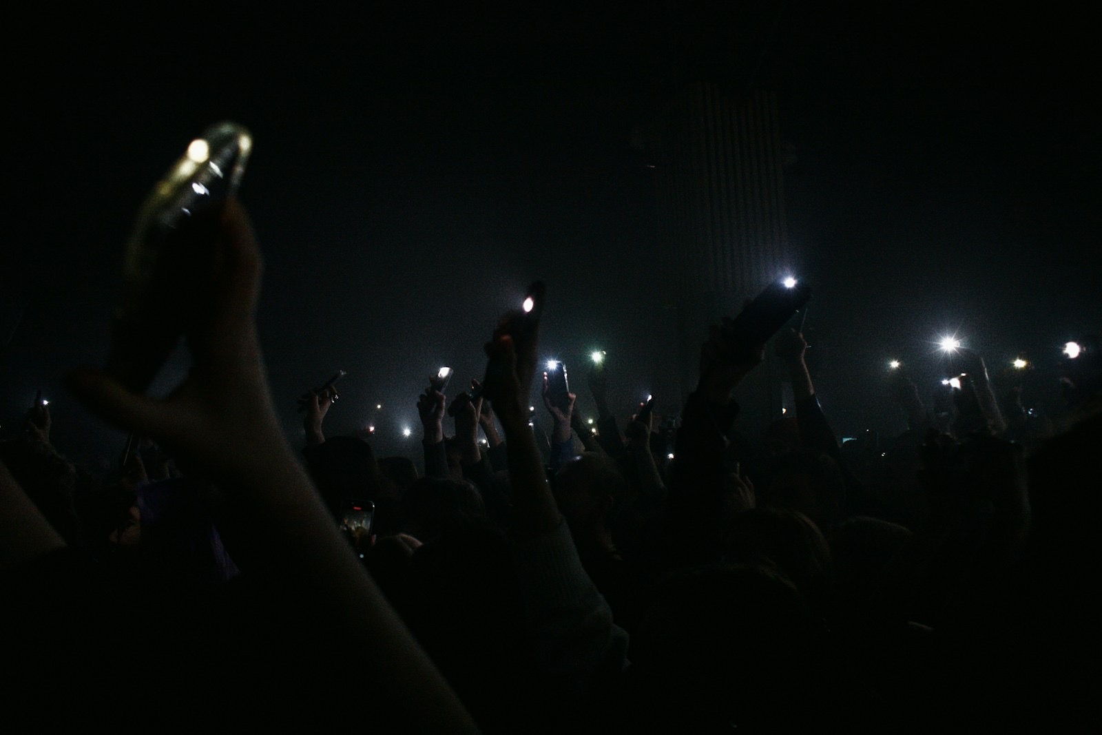Hands raised in a dark crowd, holding up glowing phone screens